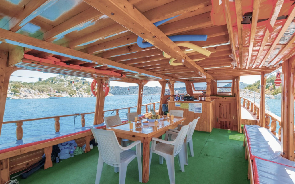 Kekova tekne turunda ahşap güvertede yemek masası ve içeceklerle donatılmış sosyal alan